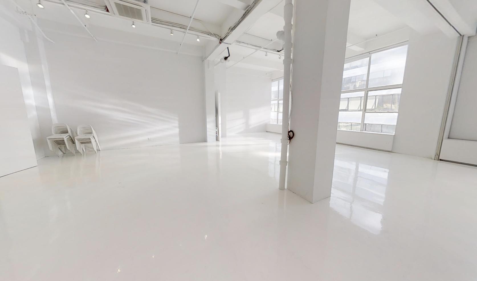 An event venue with white floors, high ceilings, large windows, and stacked chairs at Location 05.
