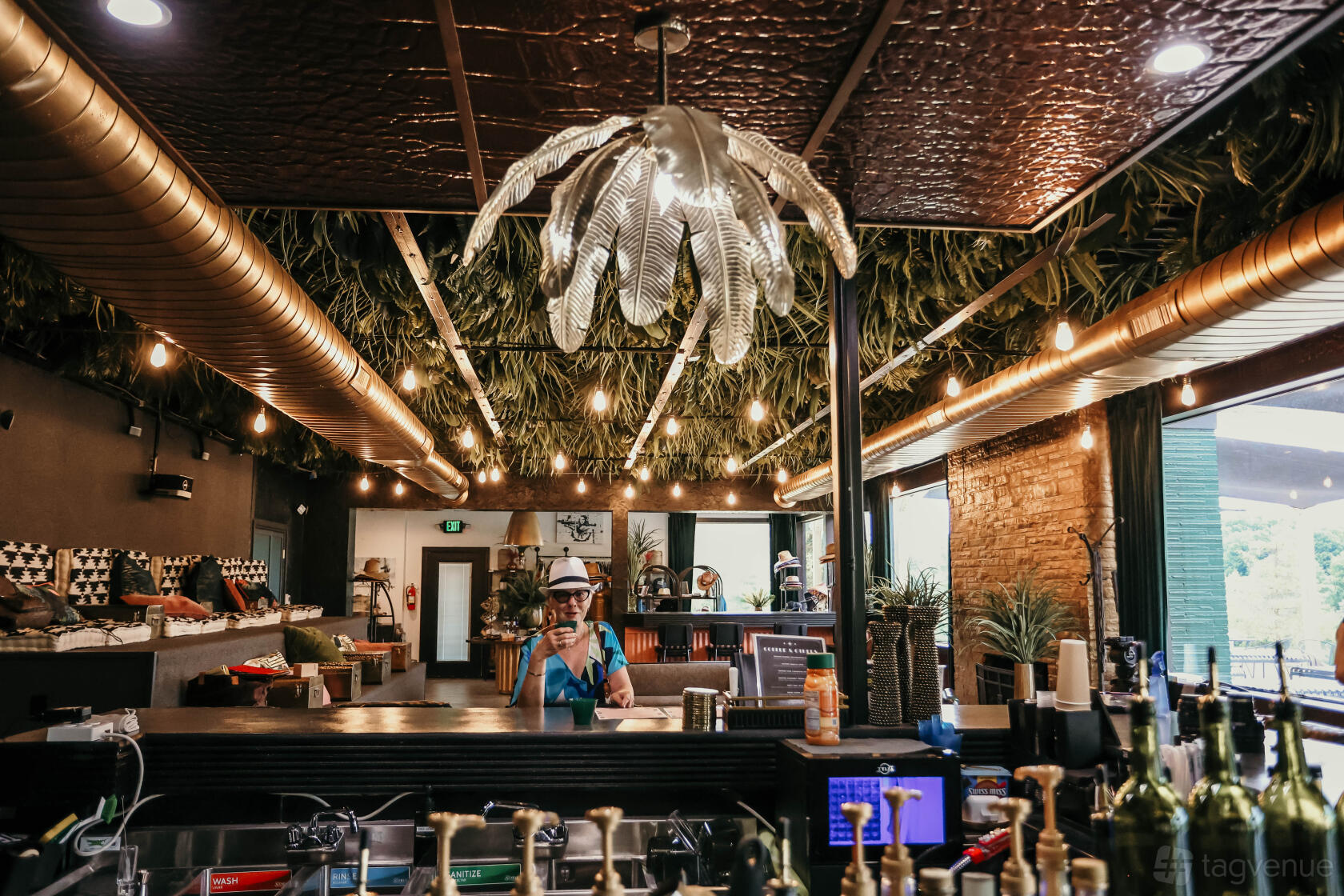 An event space with a leafy ceiling installation, string lighting, and a central bar at DayDreamer Domes.