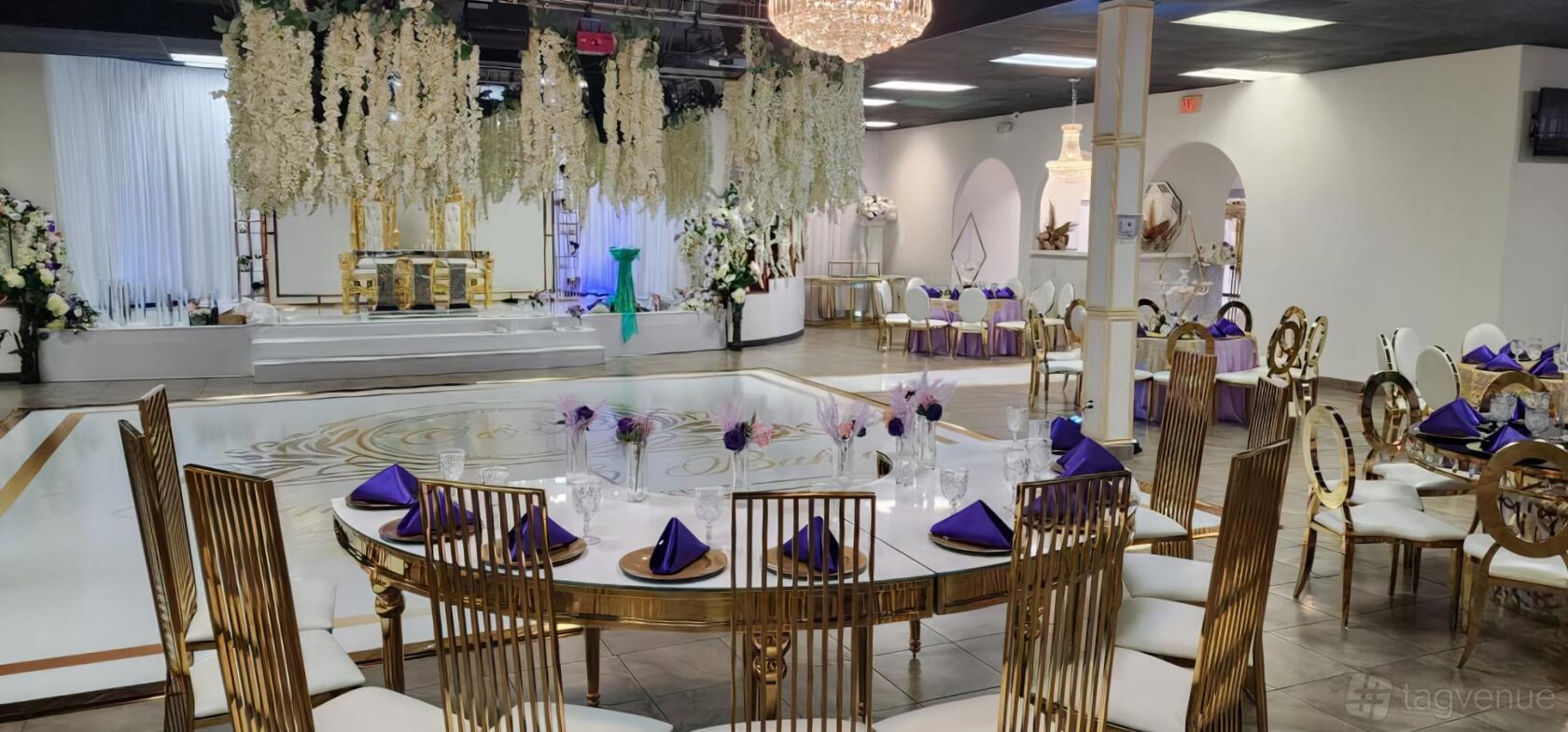 A hall with gold chairs, a polished dance floor, floral ceiling decor, and chandelier lighting at Bam Bam Reception Hall.