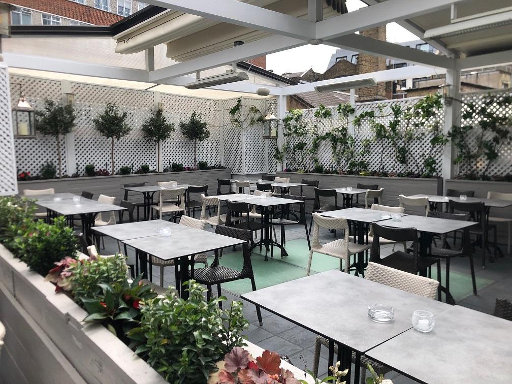 A rooftop restaurant with white lattice walls, potted plants, and outdoor dining tables at The Elysee.