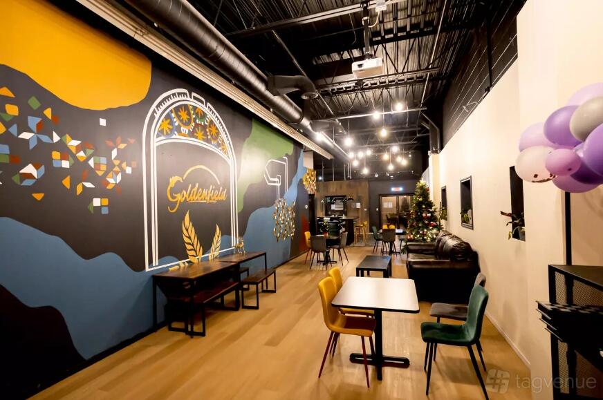An event space with colorful wall murals, exposed ceilings, mixed seating, and string lights at Goldenfield Brewery.