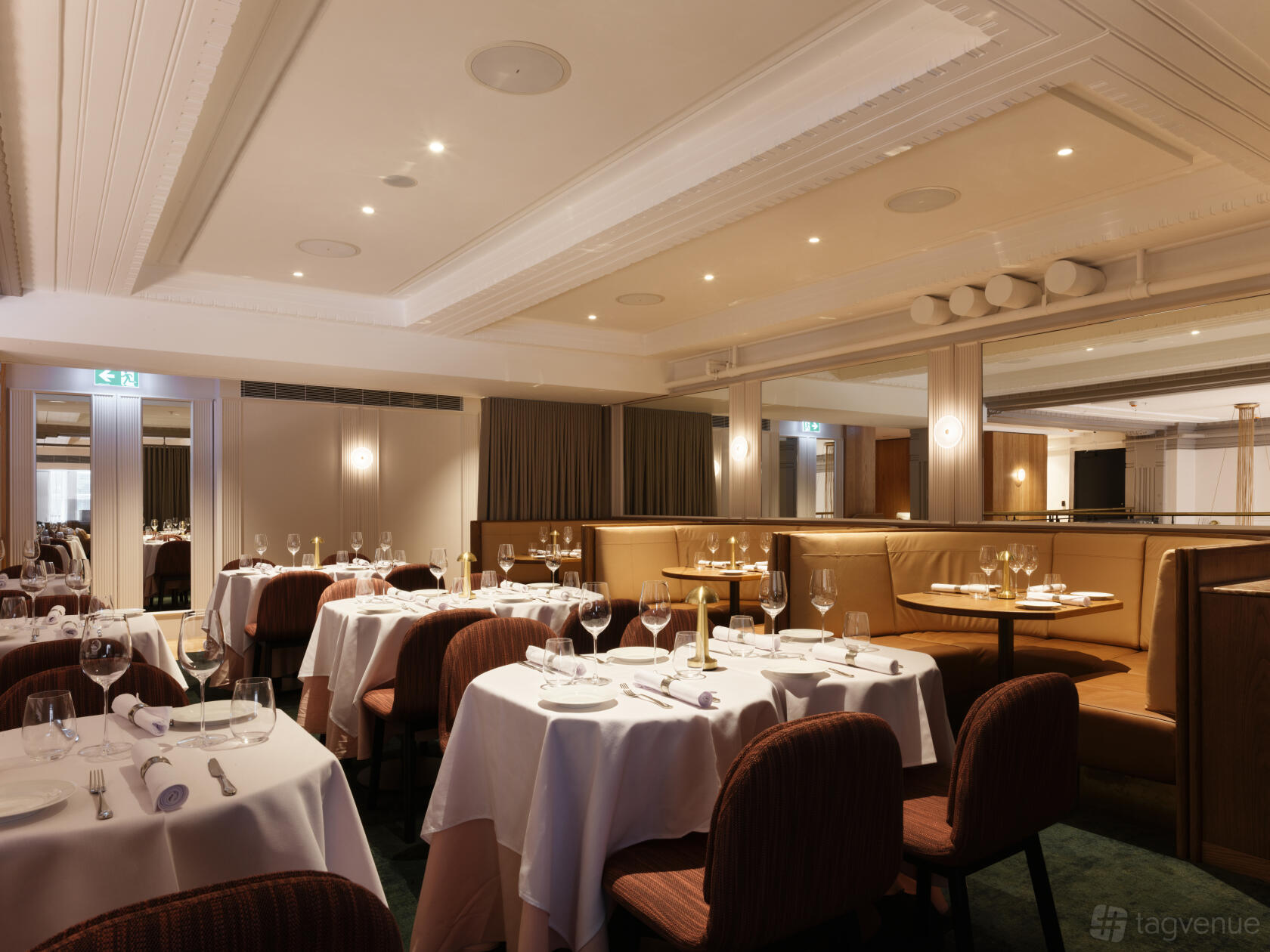 A dining room with round tables covered in white linens, upholstered chairs, and booth seating at The Charles Grand Brasserie.