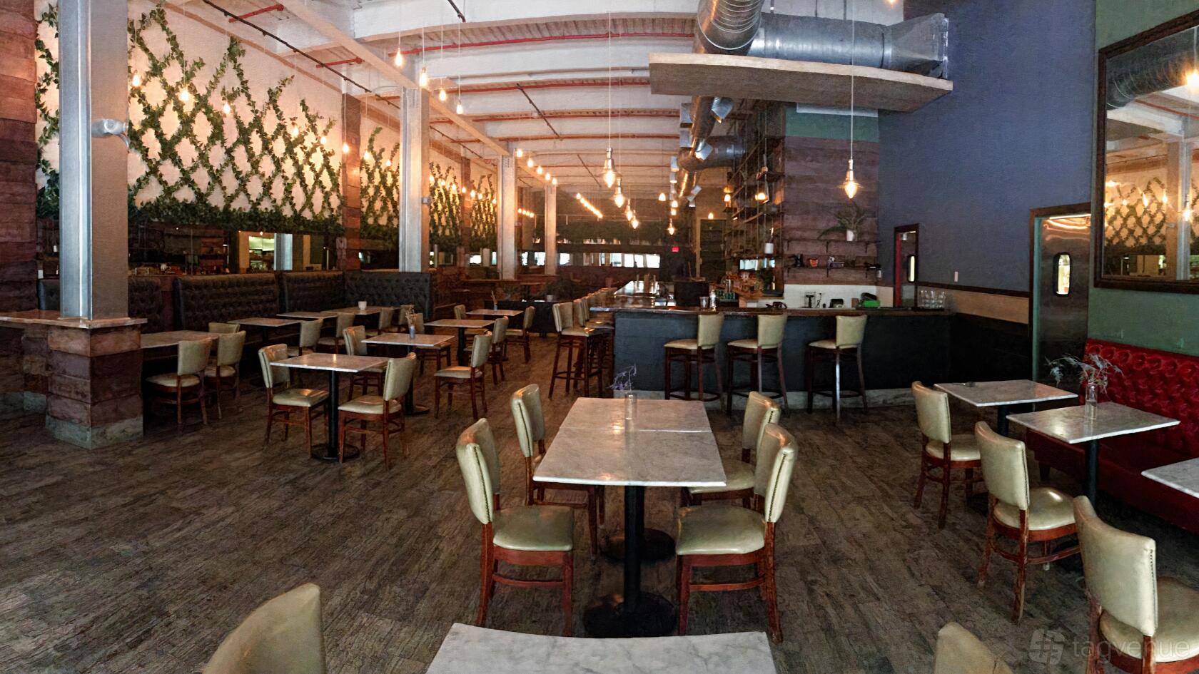 An event space in a restaurant with marble-top tables, tufted banquettes, and greenery-covered walls at Woodside.