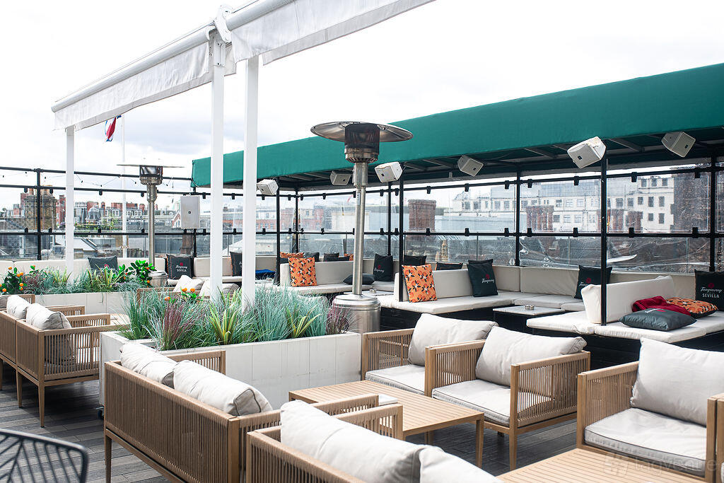 A rooftop terrace with cushioned lounge seating, wooden tables, potted plants, and city views at Courthouse Hotel Soho.
