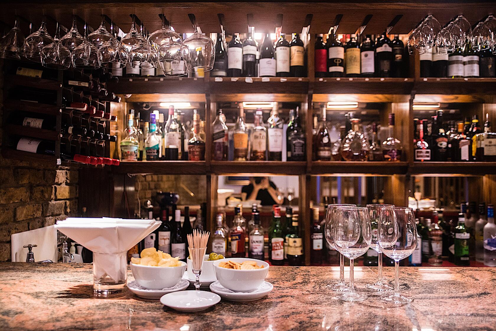 A restaurant with a marble bar counter, glassware, and shelves of wine and spirits at Bolton's.