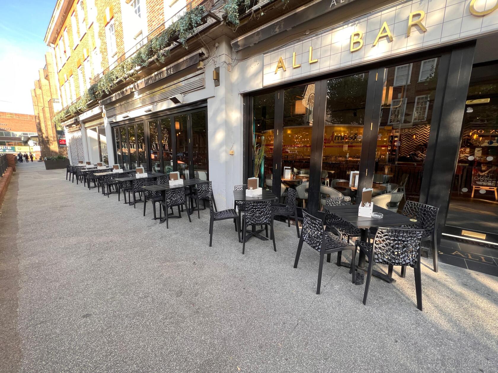 A bar with outdoor seating featuring black tables and chairs along the sidewalk at All Bar One Sutton.