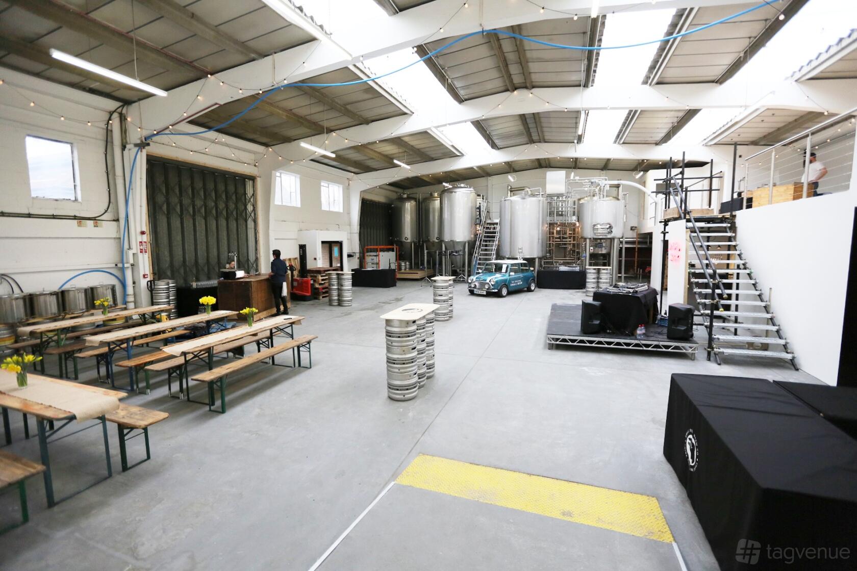 A spacious brewery bar with picnic tables, large brewing tanks, and industrial lighting at Small Beer Brew Co.