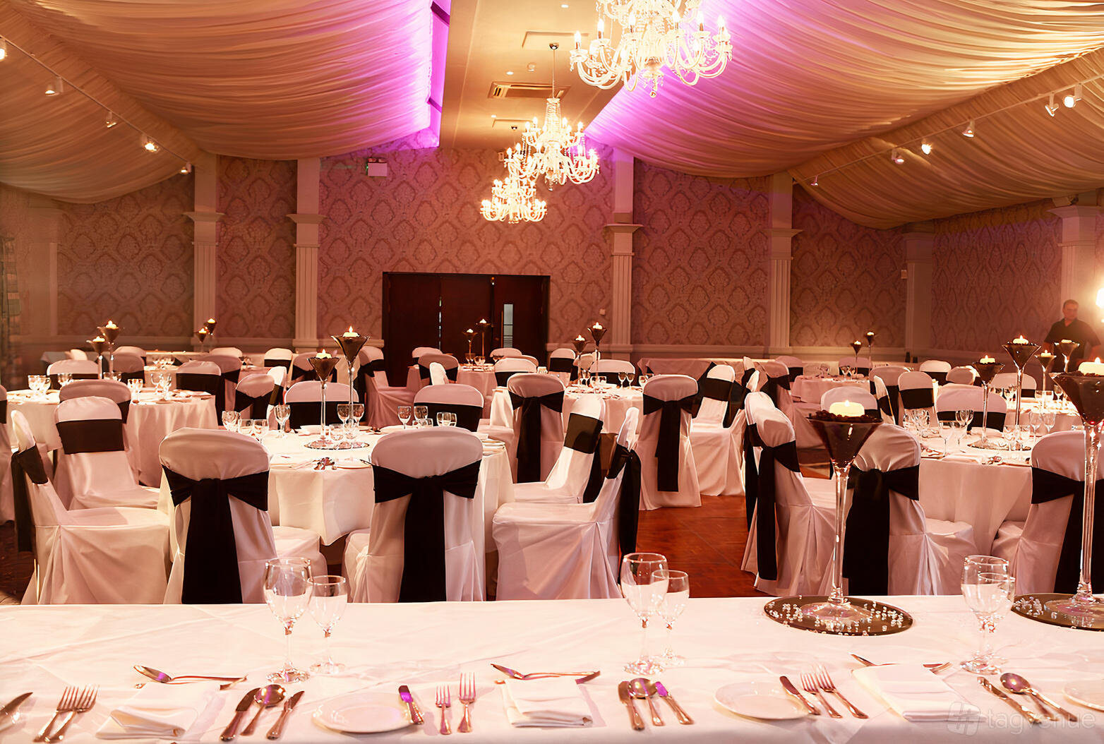 An event space with draped fabric ceiling, chandeliers, and round tables dressed in white linens at Keavil House Hotel.
