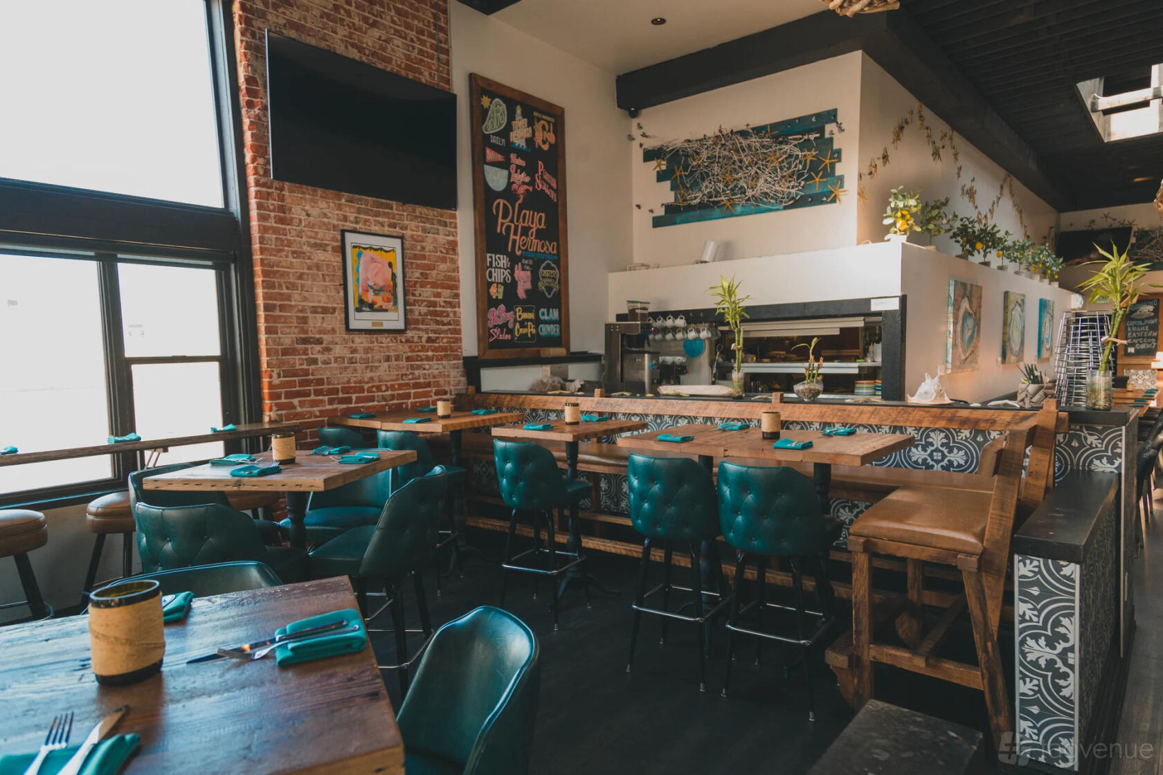 An event space in a restaurant with teal tufted chairs, exposed brick walls, and wall art at Playa Hermosa Fish & Oyster Co.