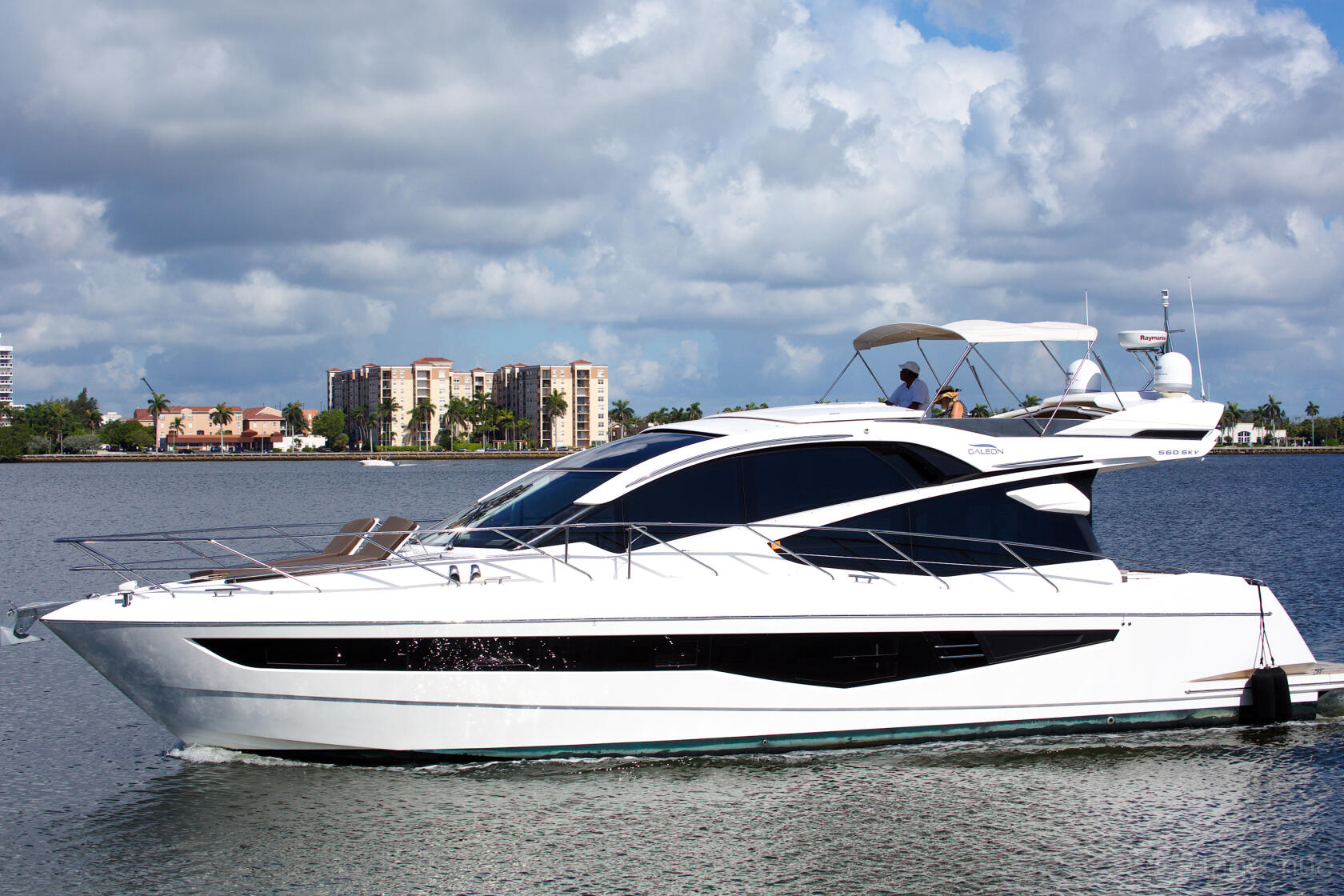 A sleek white yacht with large windows and an upper deck cruising on the water at Lots Of Yachts/Lots Of Spots South Florida.