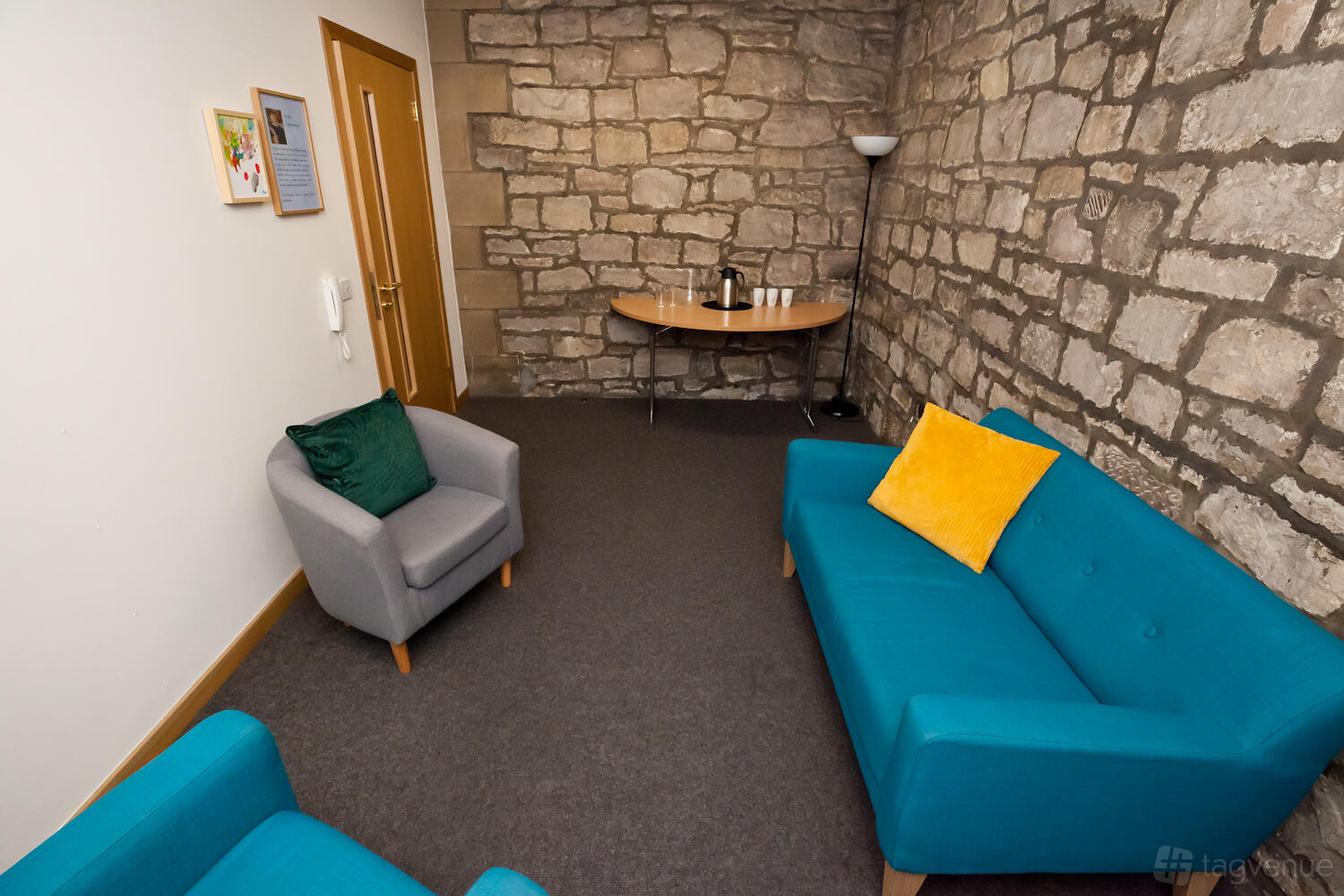 A conference centre lounge with exposed stone walls, teal sofas, and a refreshment table at Norton Park Conference Centre.