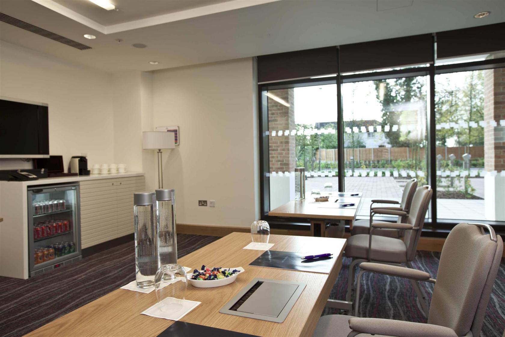 A hotel meeting room with floor-to-ceiling windows, modern chairs, and a refreshment counter at Hilton London Heathrow Airport Terminal 5.