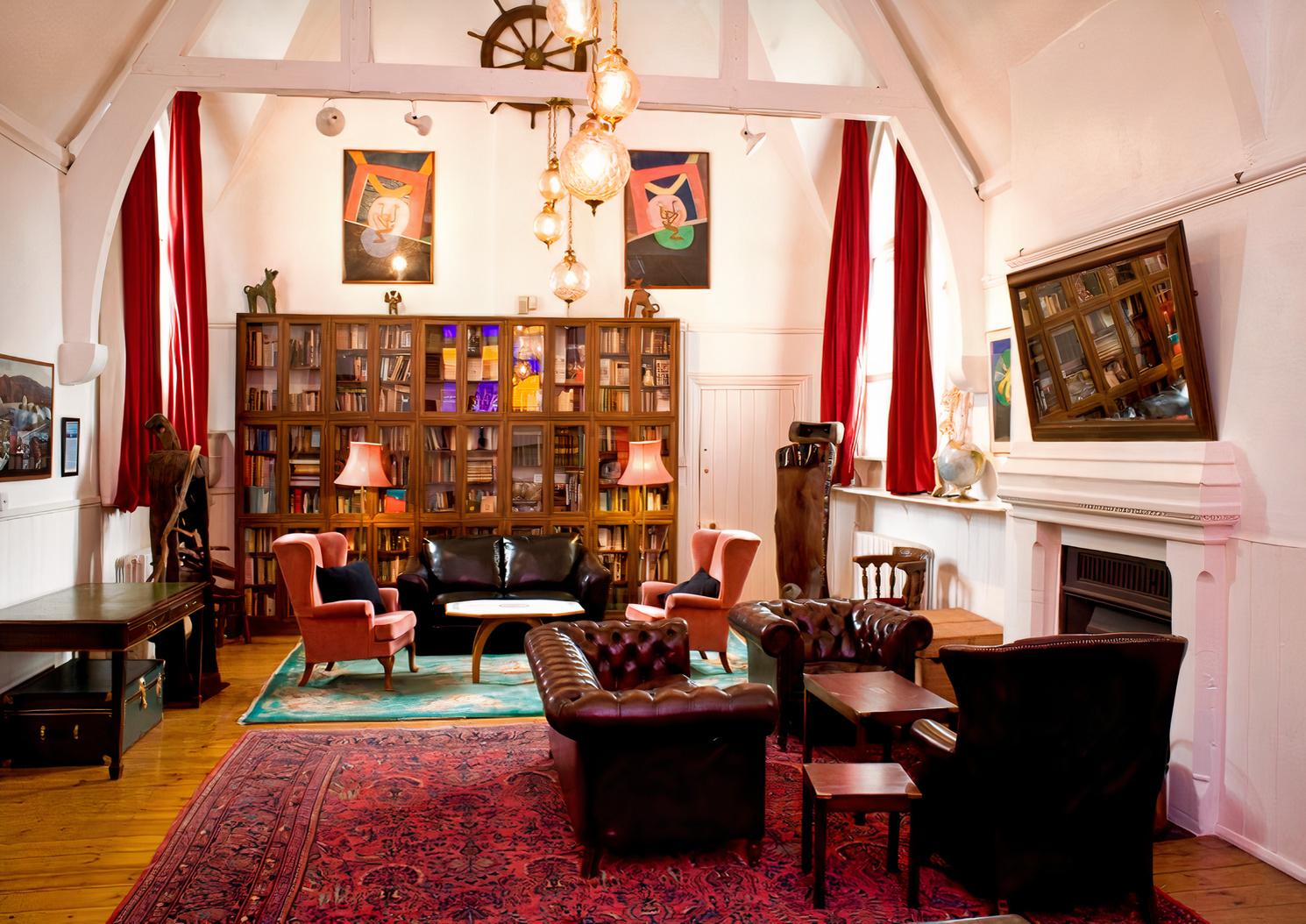 A gallery lounge with high arched ceilings, leather seating, bookshelves, and large windows at October Gallery.
