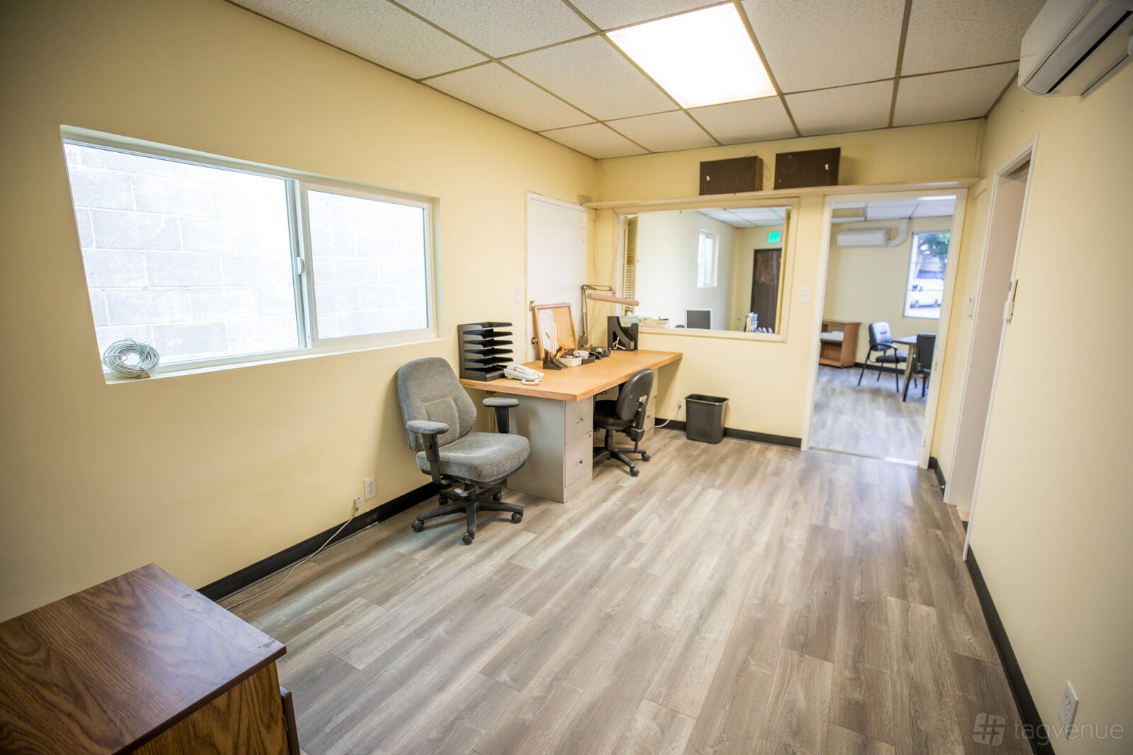 A meeting room with desks, office chairs, wood-style flooring, and a large window at PodShare - Culver City Affordable Office.