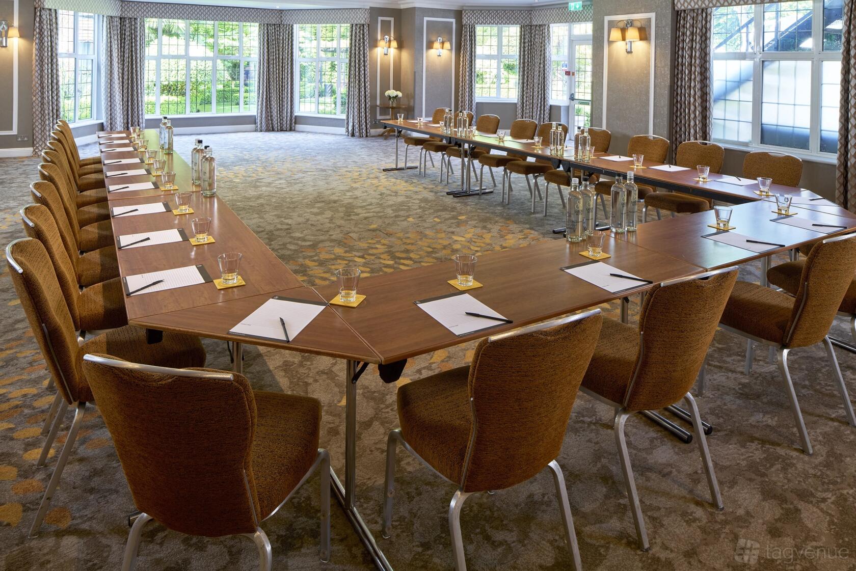 An event space with floor-to-ceiling windows, patterned carpet, and U-shaped tables set for meetings at The Bull Hotel.
