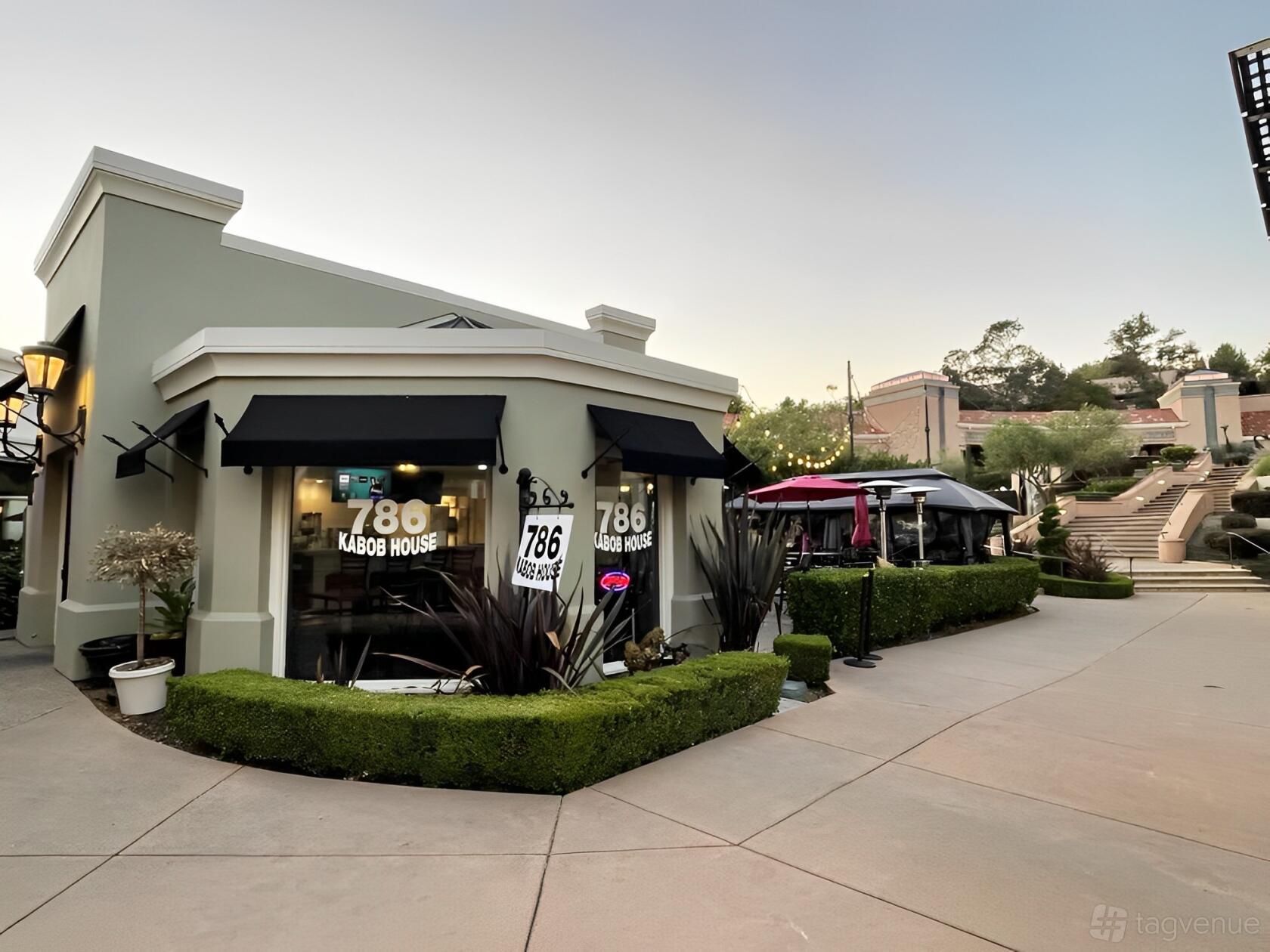 A restaurant with black awnings, large windows, and trimmed hedges at 786 Kabob House.