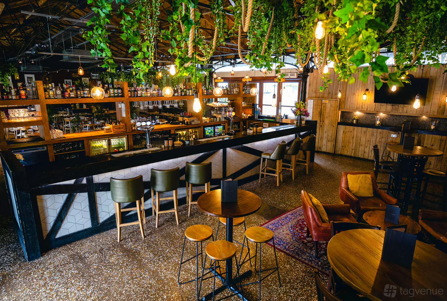 A bar in a restaurant with hanging greenery, pendant lights, and wood accents at Harbour House.