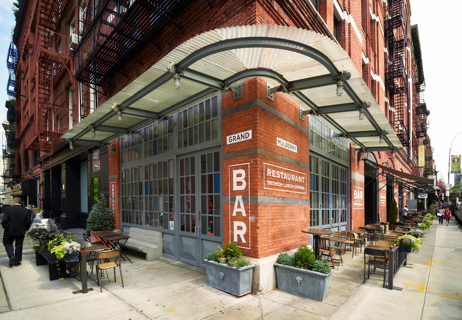 A restaurant with sidewalk seating, potted plants, and large glass windows at Gelso & Grand.