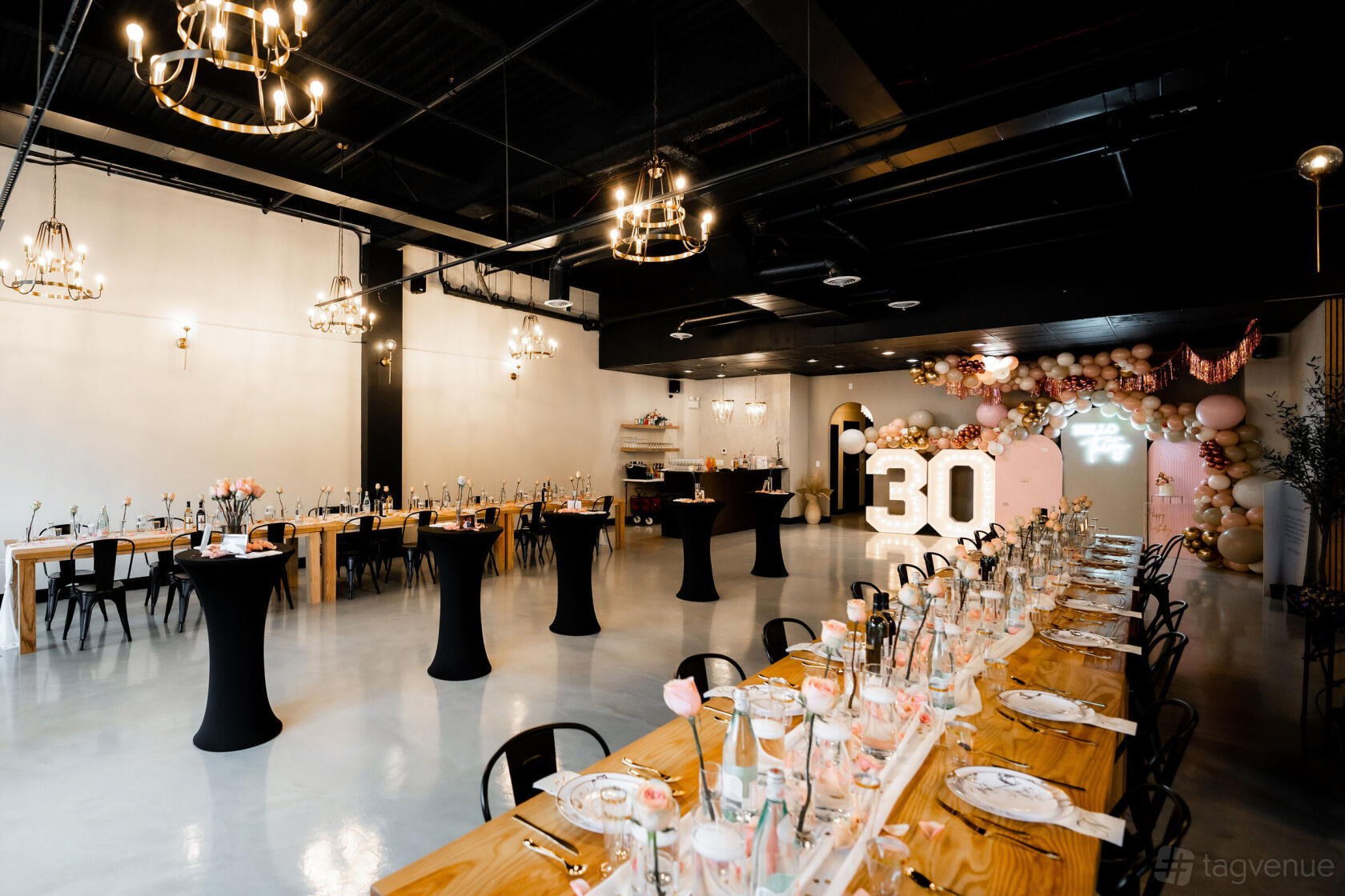 A loft with high ceilings, chandeliers, polished floors, long banquet tables, and balloon decorations at The Social Loft.