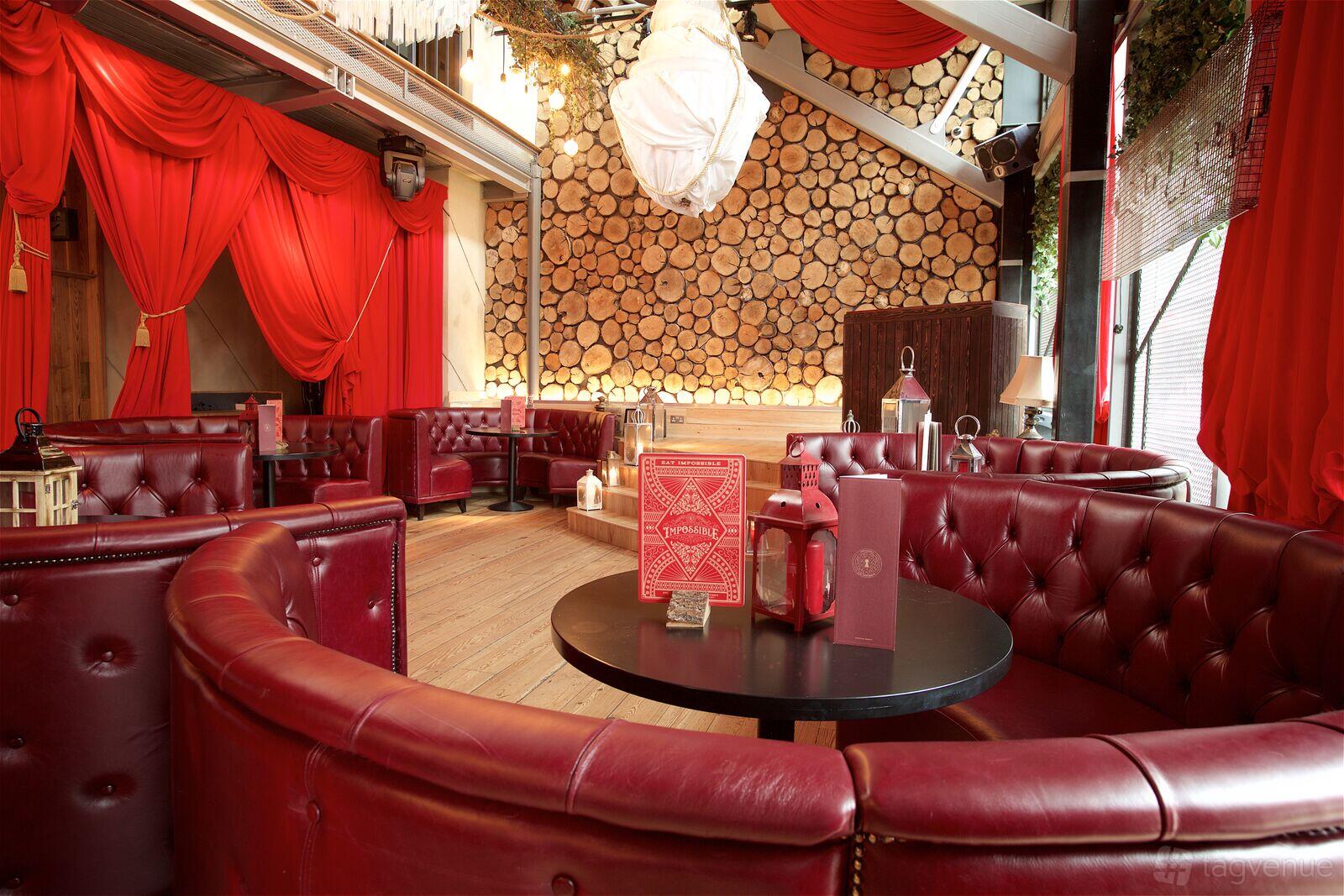 A bar with red leather banquette seating, log stack walls, and draped red curtains at Impossible Bar and Theatre.
