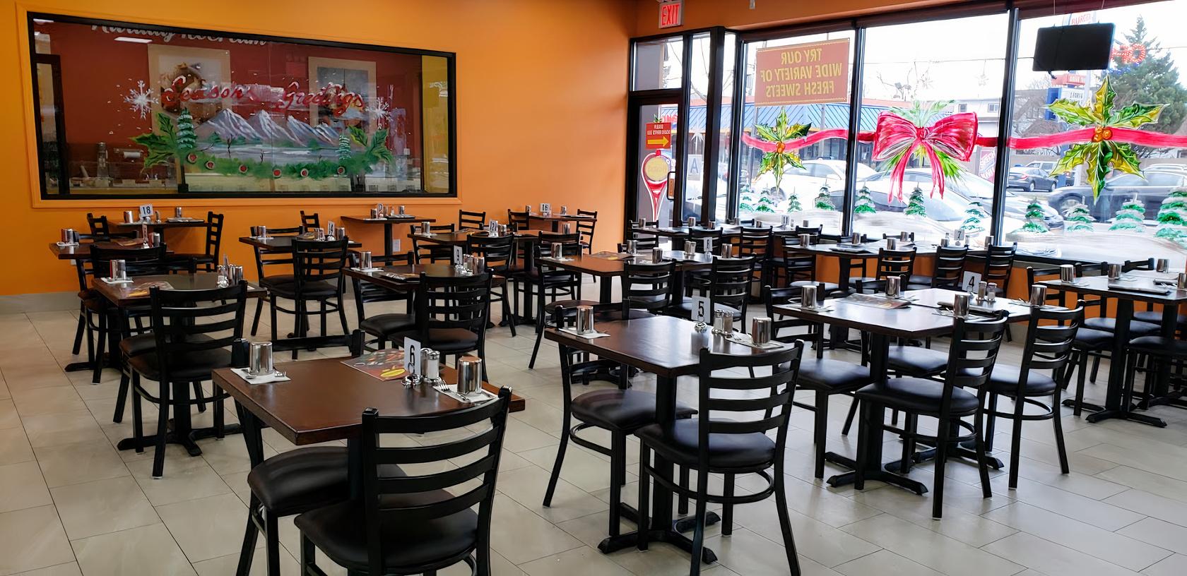 A restaurant dining area with dark wooden tables, black chairs, and large street-facing windows at Honest Indian Restaurant.