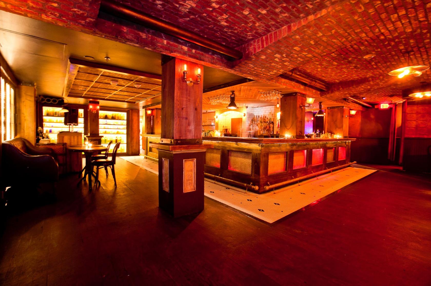A nightclub with exposed brick ceilings, dim lighting, a wooden dance floor, and a long bar at Dirty Laundry.