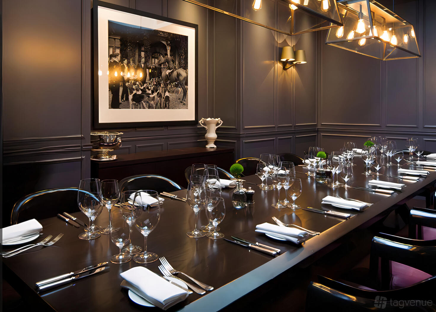 A hotel dining room with a long dark wood table, formal place settings, and wall art at London EDITION.