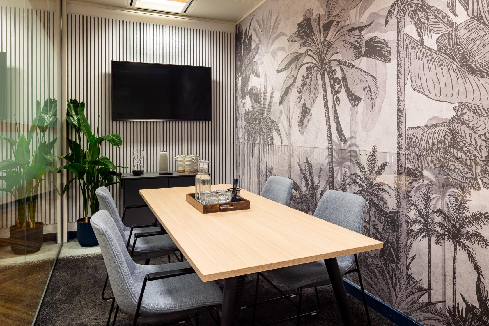 A meeting room with a wooden table, grey chairs, palm tree wall mural, and a TV at Landmark: Gracechurch Street, London.