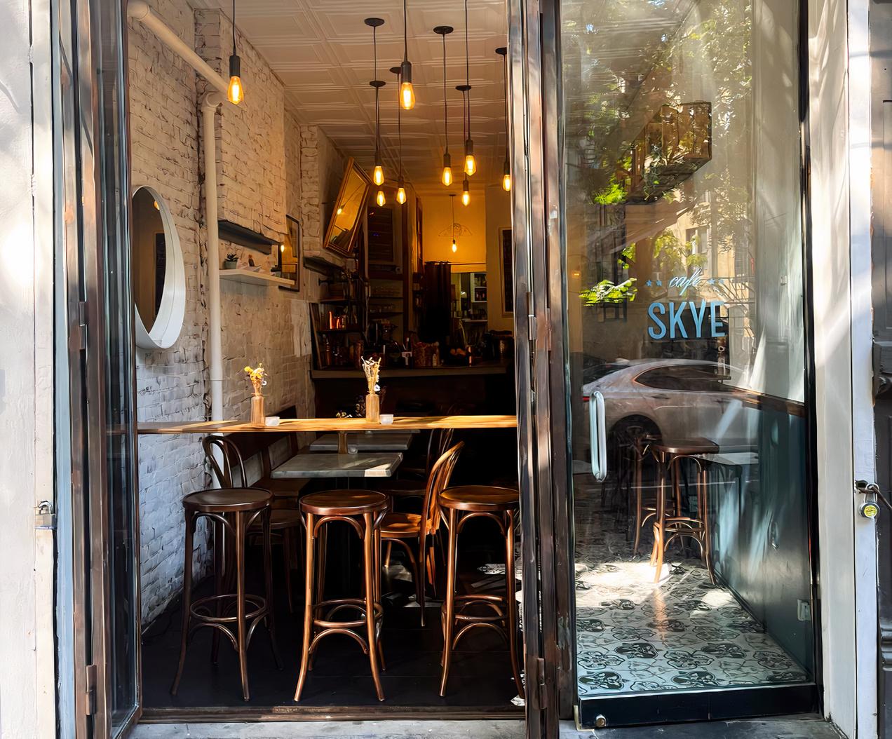 A café with exposed white brick walls, hanging pendant lights, and round wooden chairs at Cafe Skye.
