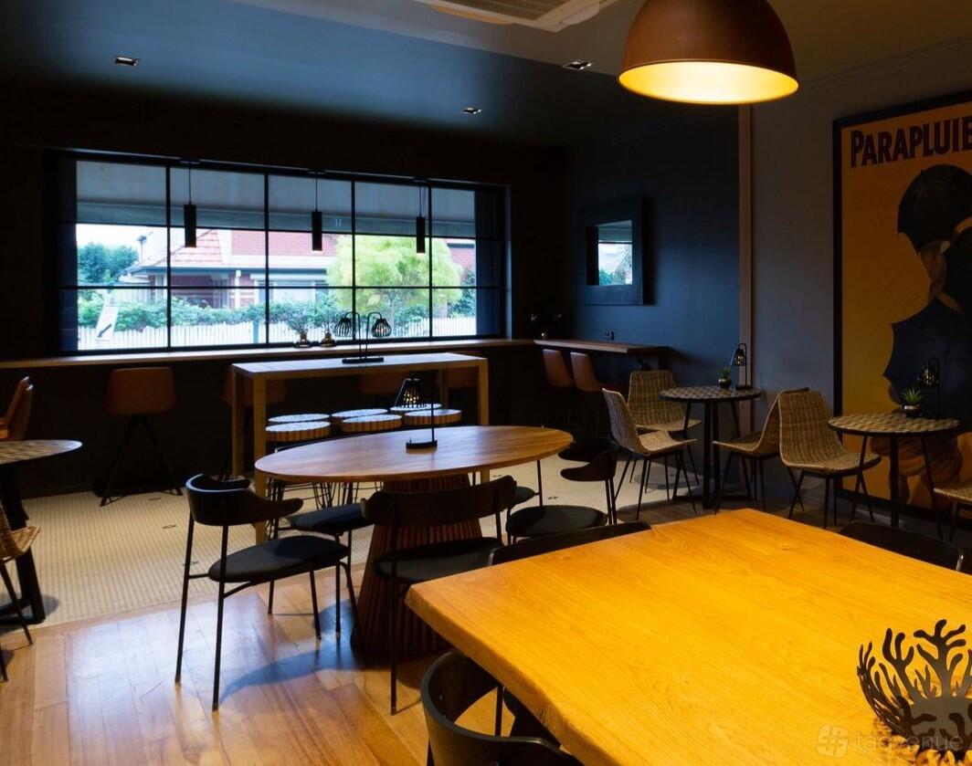 A bar with round wooden tables, woven chairs, and large windows at Primrose & Vine.