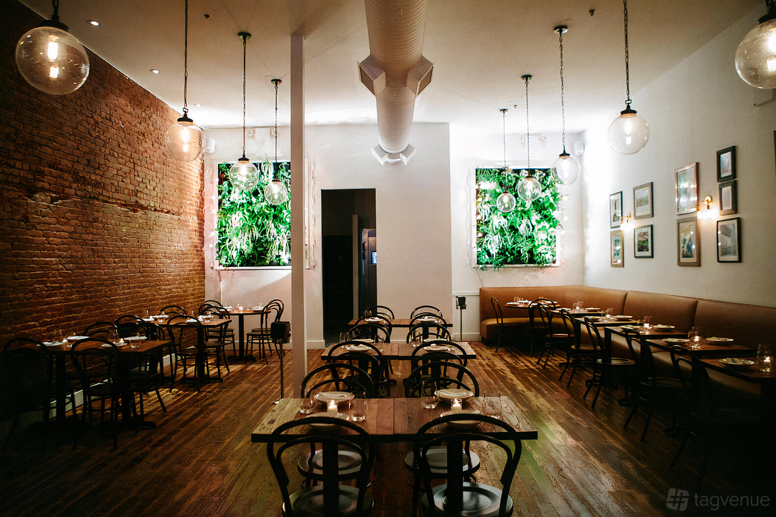 A restaurant with exposed brick walls, wooden floors, greenery panels, and globe pendant lights at Gran Morsi.