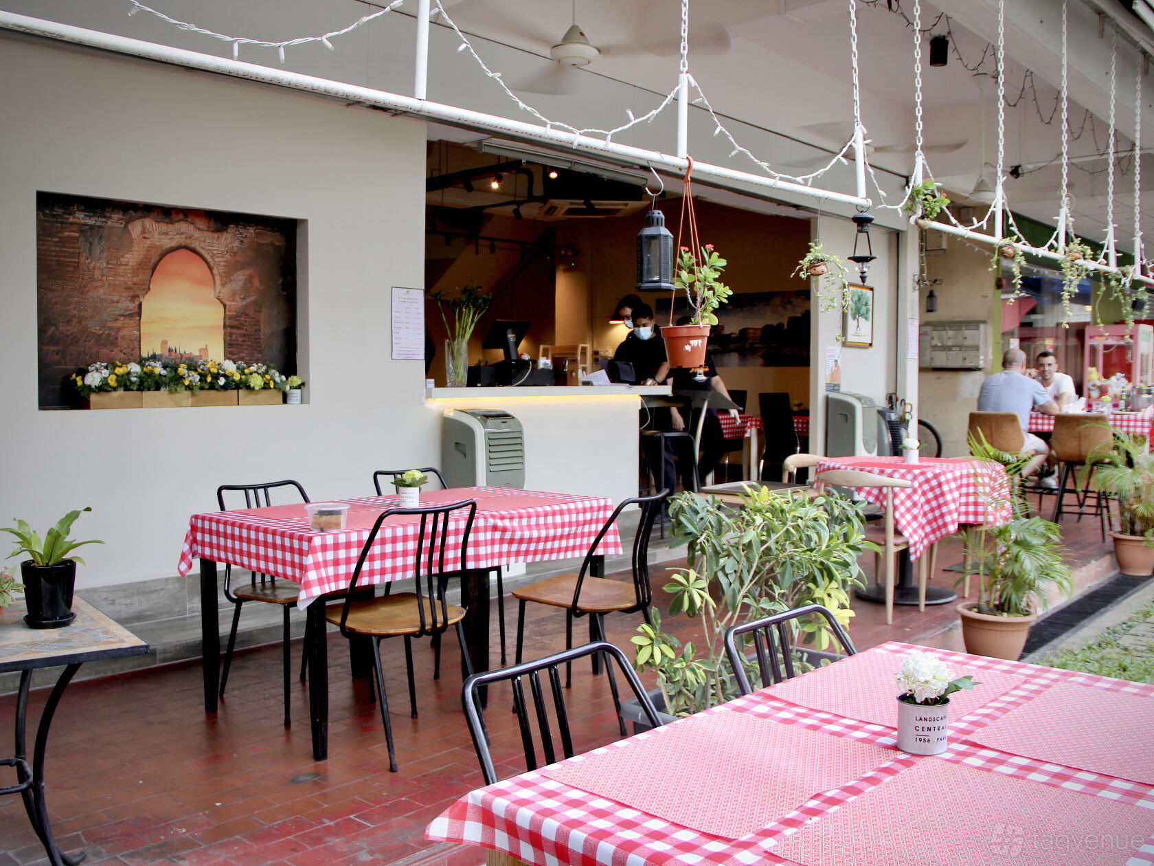 An open-air restaurant with red checkered tablecloths, potted plants, and hanging lights at Micasa Kitchen and Bar.