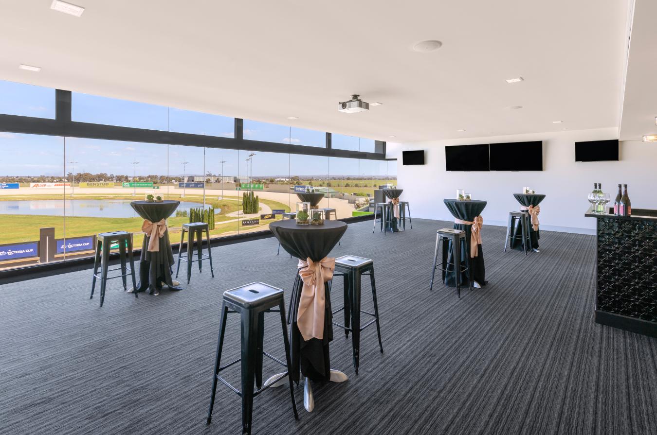 An event venue with floor-to-ceiling windows, cocktail tables, and racecourse views at Melton Entertainment Park.