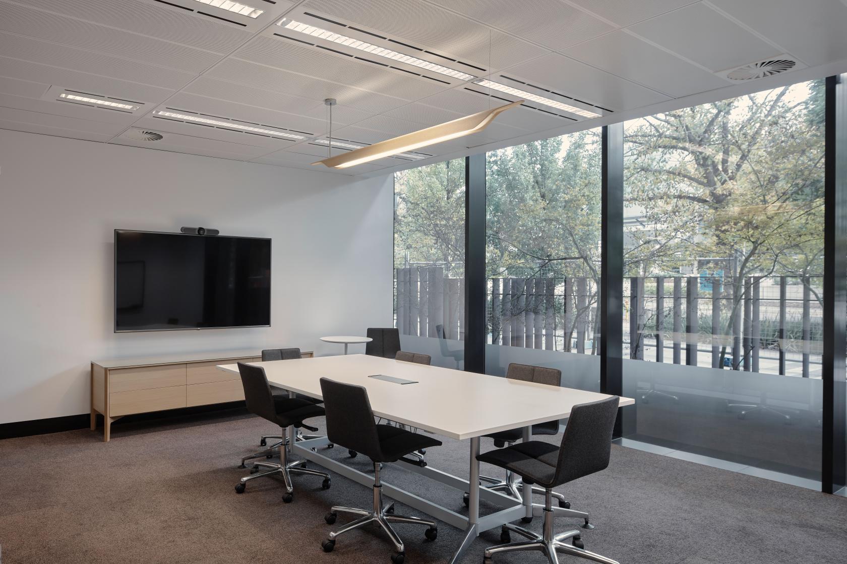 A meeting room with floor-to-ceiling windows, a large screen, and a white conference table at Flex by ISPT at 4 National Circuit.