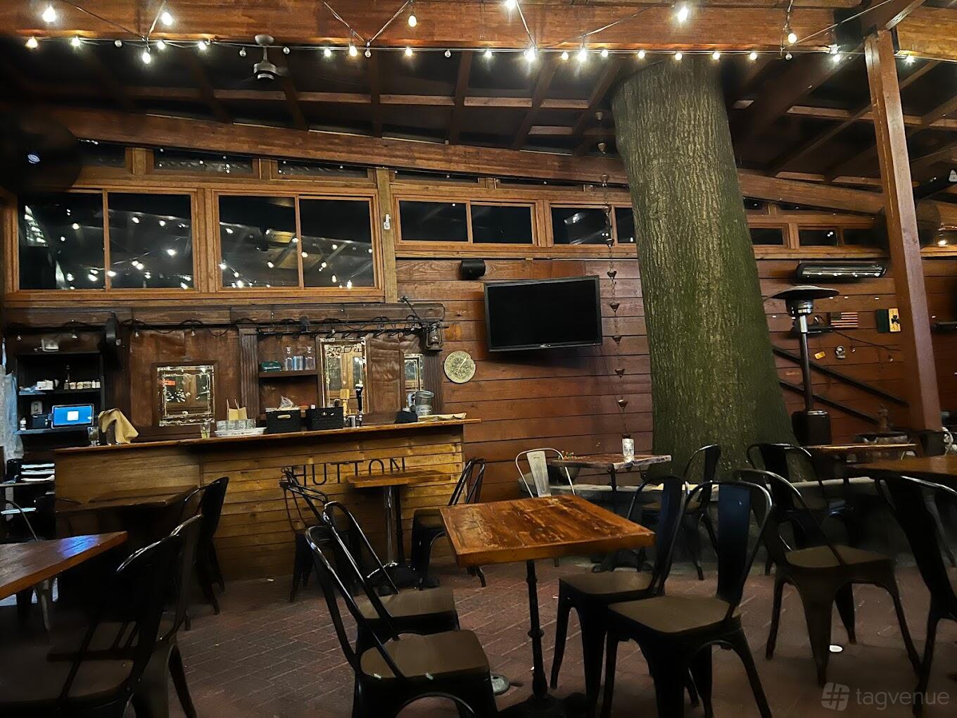 A restaurant with wood-paneled walls, a rustic bar, exposed beams, and string lights at The Hutton Restaurant and Bar.