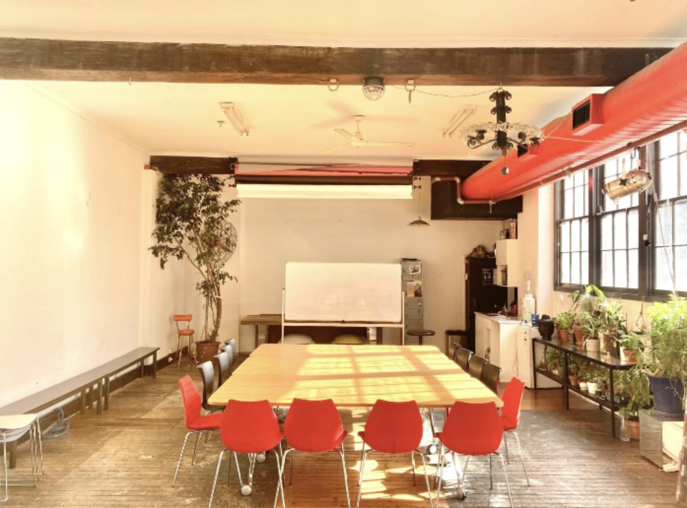 A warehouse creative space with red chairs around a large table, potted plants, and tall windows at San Telmo Studio.