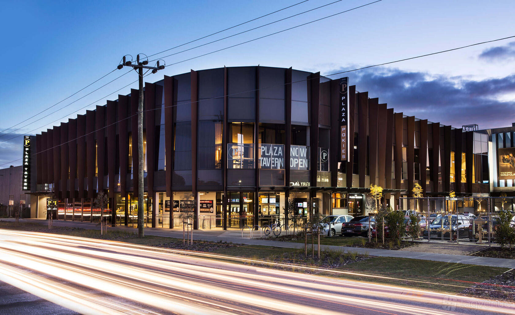 A hotel exterior with modern angular facade, large glass windows, and illuminated signage at Plaza Tavern - Werribee.