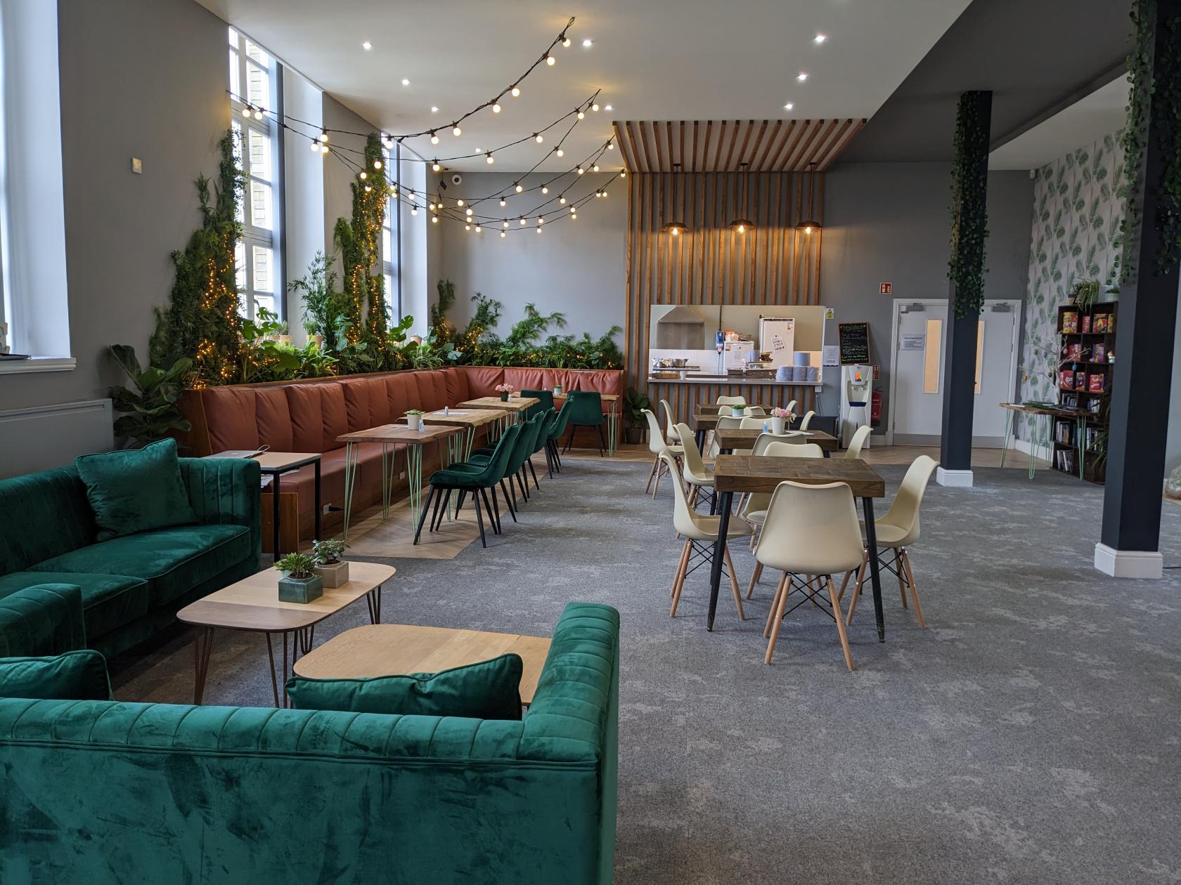 An event venue with green velvet sofas, wood tables, string lights, and plant accents at Jubilee Centre Lettings.
