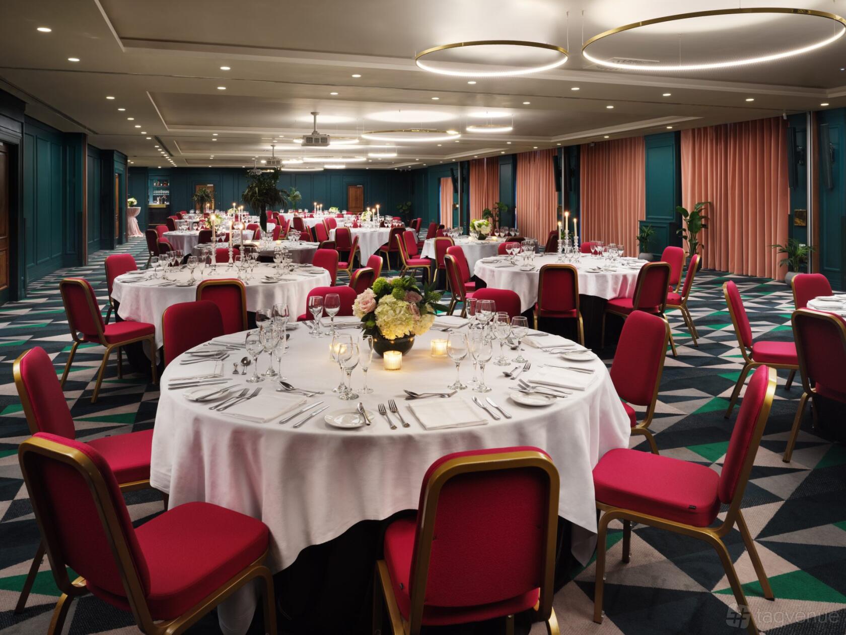 An event space with round tables covered in white linens, red chairs, and geometric carpet at The Alex Hotel.