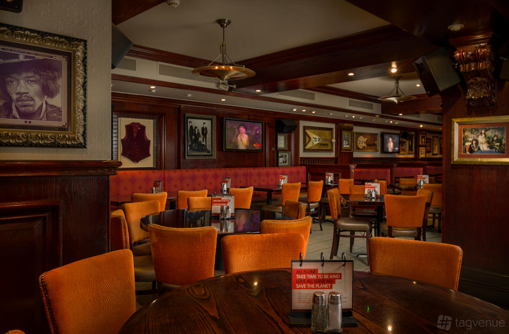 A restaurant dining area with orange cushioned chairs, round dark wood tables, and music memorabilia at Hard Rock Cafe Edinburgh.