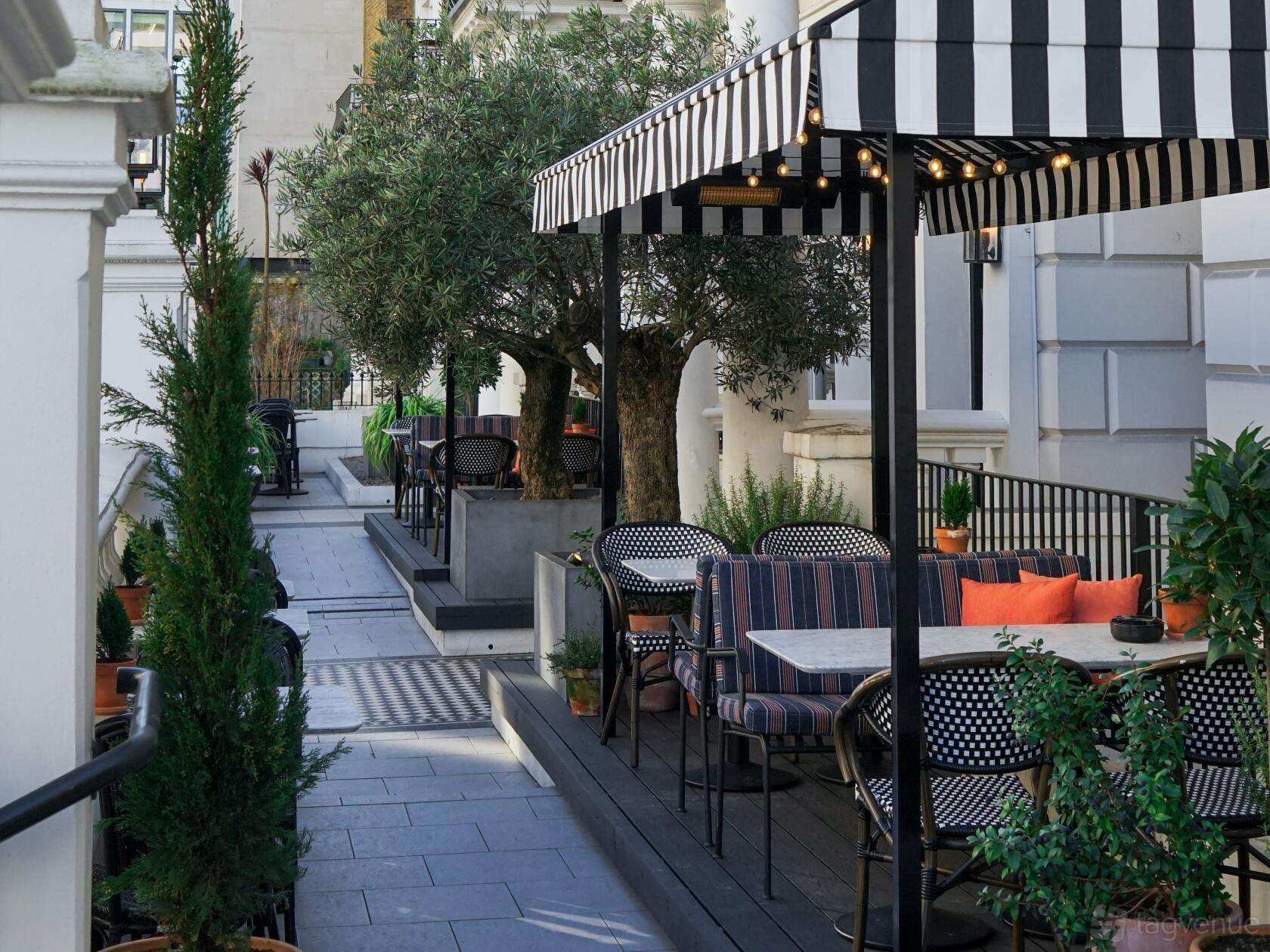 A terrace with striped awnings, potted plants, and black café tables with striped chairs at The Laslett.