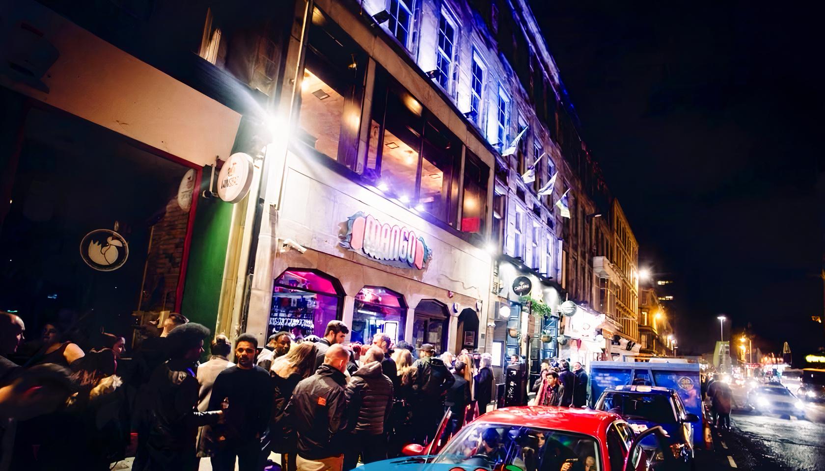 A nightclub exterior with a lit façade, neon signage, and a crowd gathered outside at Mango Latino.