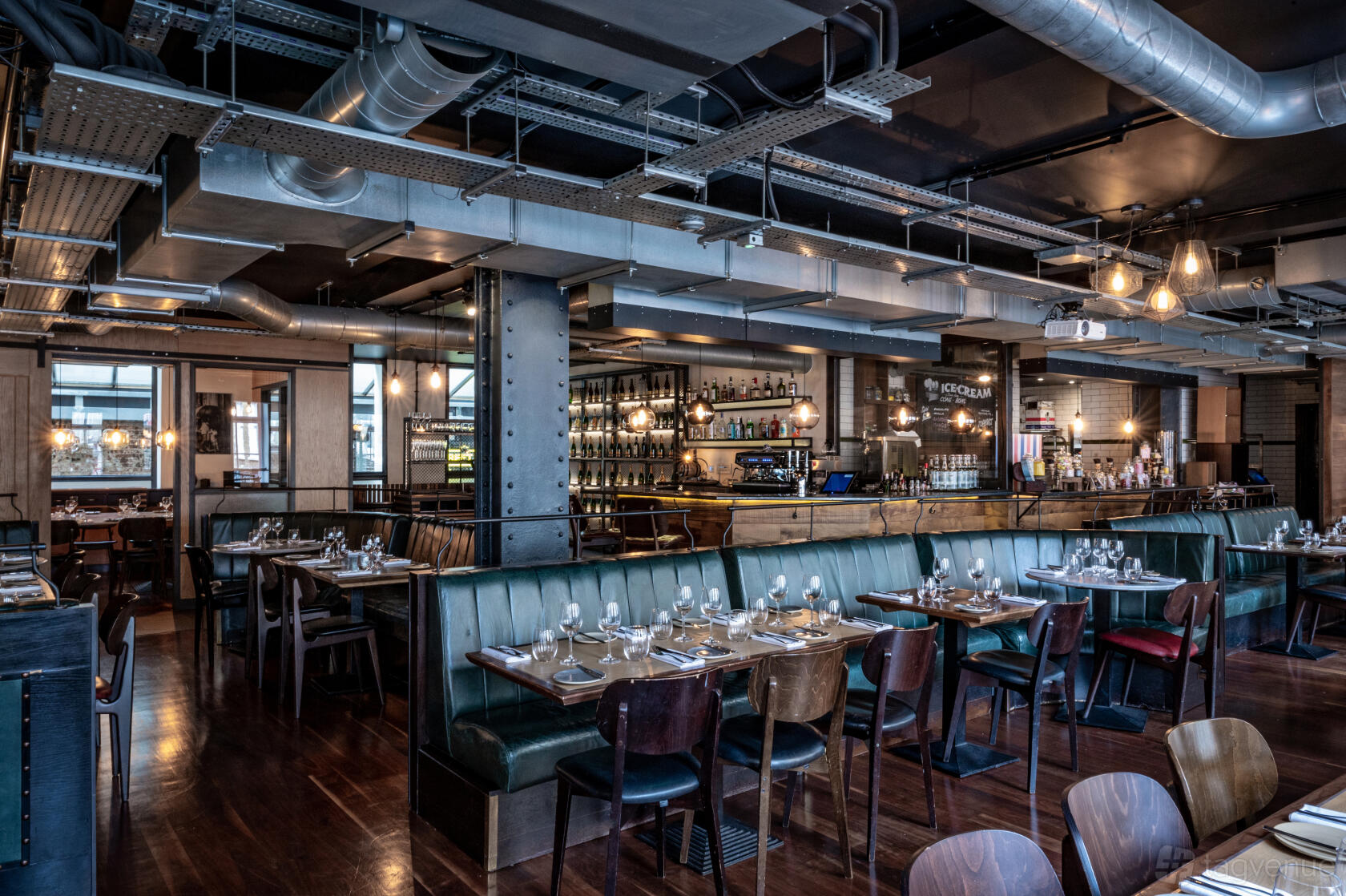 An event space in a restaurant with dark wood floors, green leather banquettes, and an open bar at Heddon Street Kitchen.