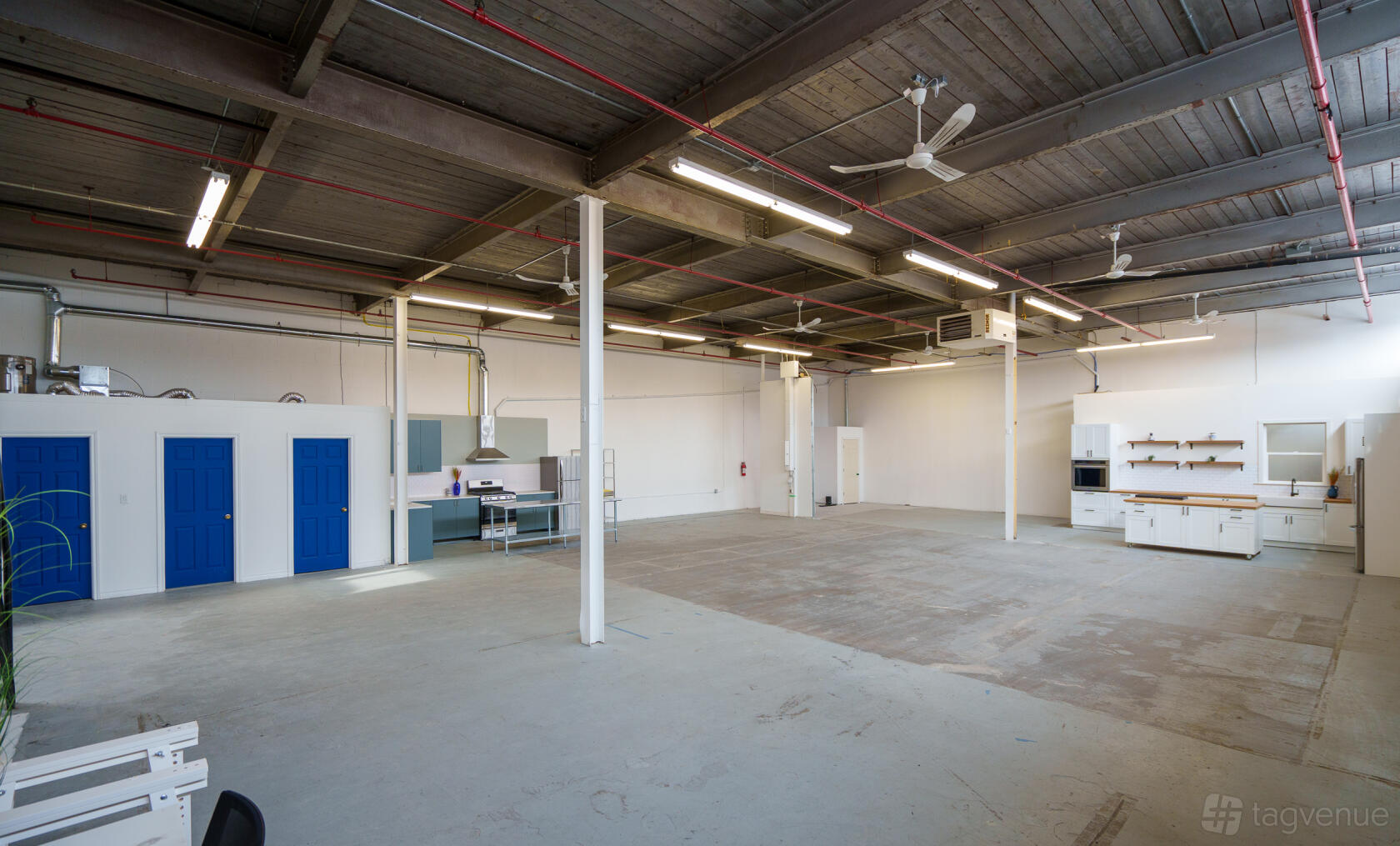A spacious photo studio with high exposed beam ceilings, concrete floors, and blue doors at Canteen Studios.