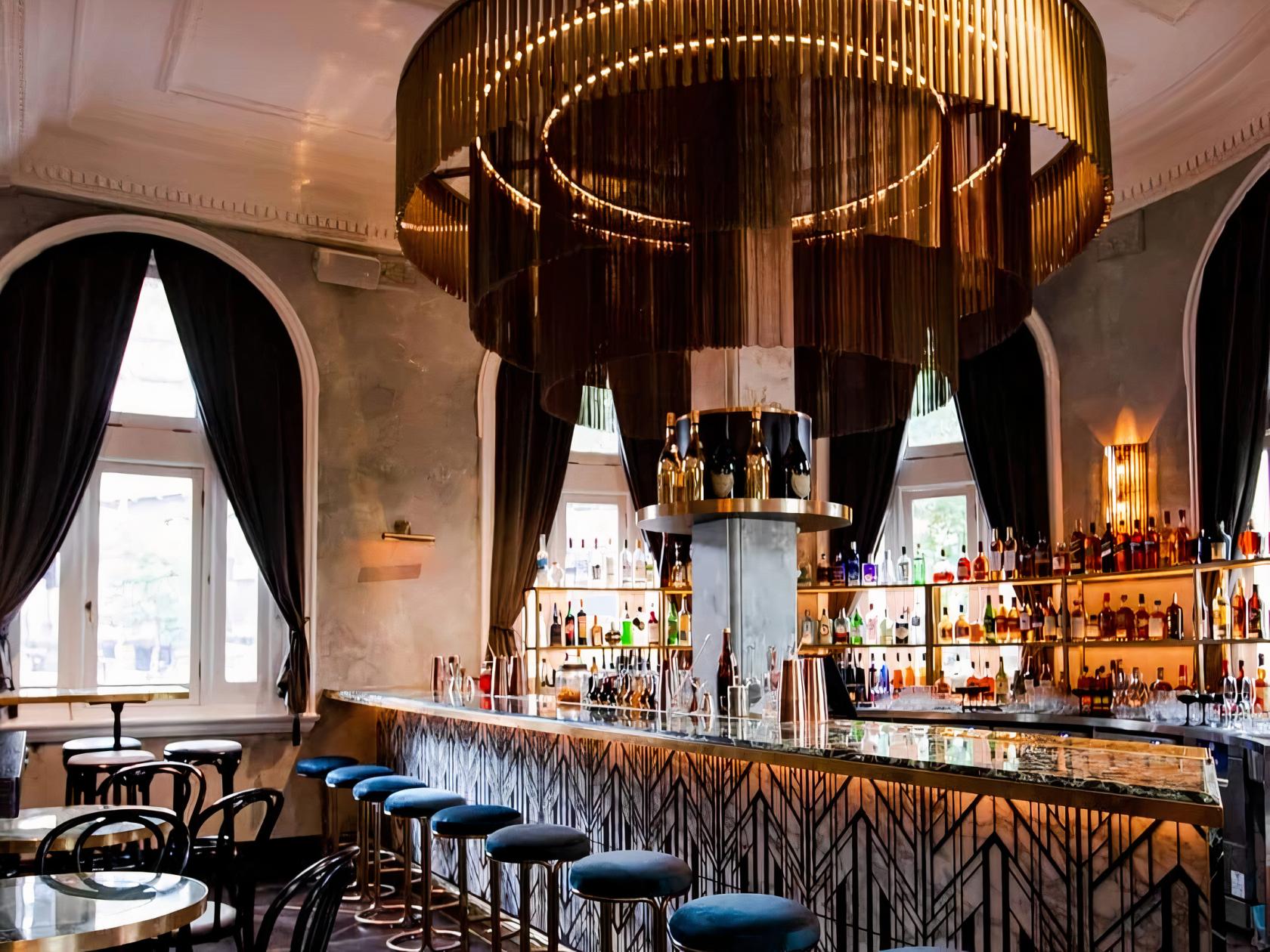 An event space in a cocktail bar with a marble-topped bar, gold chandelier, and backlit shelves at The Cat's Meow.