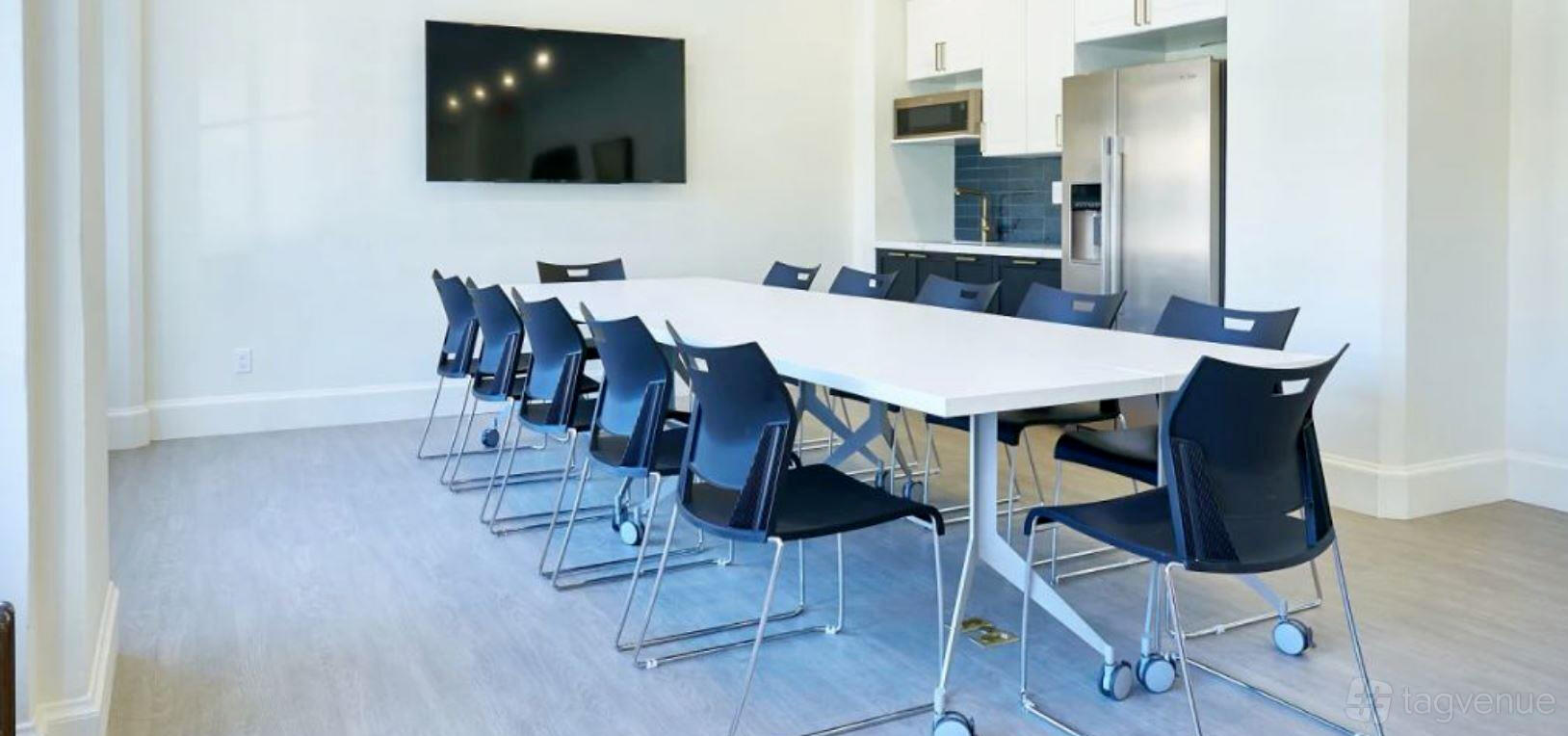 A meeting lounge with a long white conference table, black chairs on wheels, and a kitchenette at Oakstop Franklin.