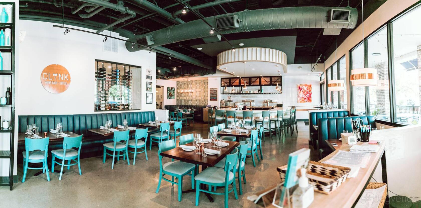 A wine bar with teal chairs, wood tables, wine display racks, and large windows at Clink Wine Bar & Bites.