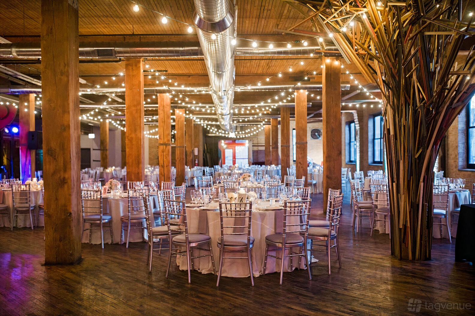 An event venue with exposed wooden beams, string lights, and round tables with white linens at Lacuna Events by LM.
