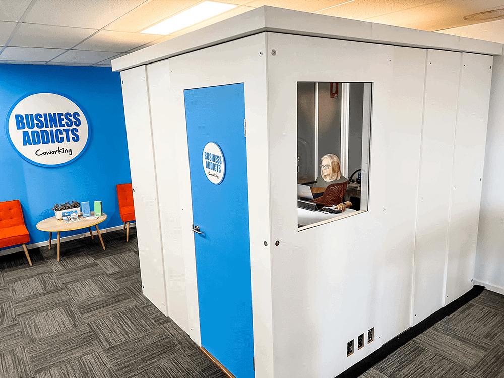 A coworking space with a soundproof recording booth featuring a blue door and interior window at Cowork + Create.