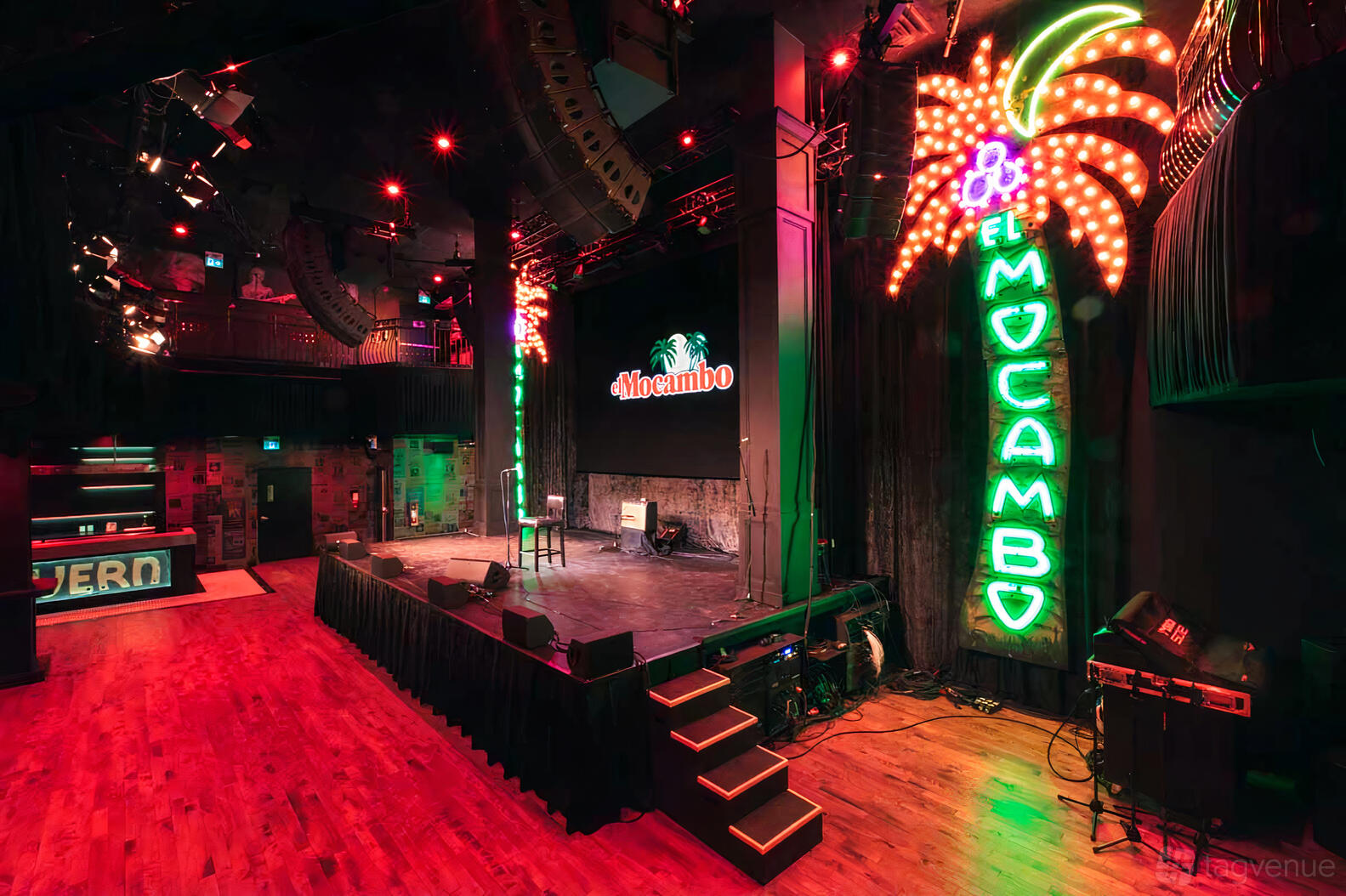 An event venue with a stage, hardwood floors, balcony seating, and neon palm tree signs at El Mocambo.